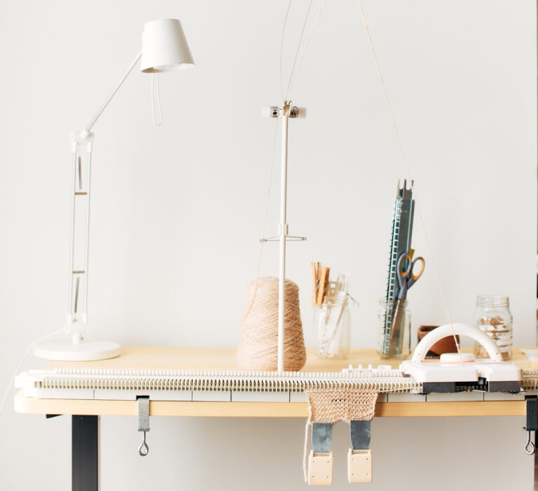 An LK150 knitting machine is mounted onto an adjustable table. A lamp sits on the left side, machine knitting tools are on the right.